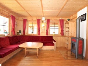 L’intérieur d’un chalet accueillant, avec un plafond en bois, des rideaux rouges, un canapé, une table et un poêle à bois.