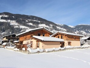 Un bâtiment de style chalet, avec une façade en bois et un toit enneigé, entouré d’un paysage couvert de neige et de montagnes en arrière-plan.