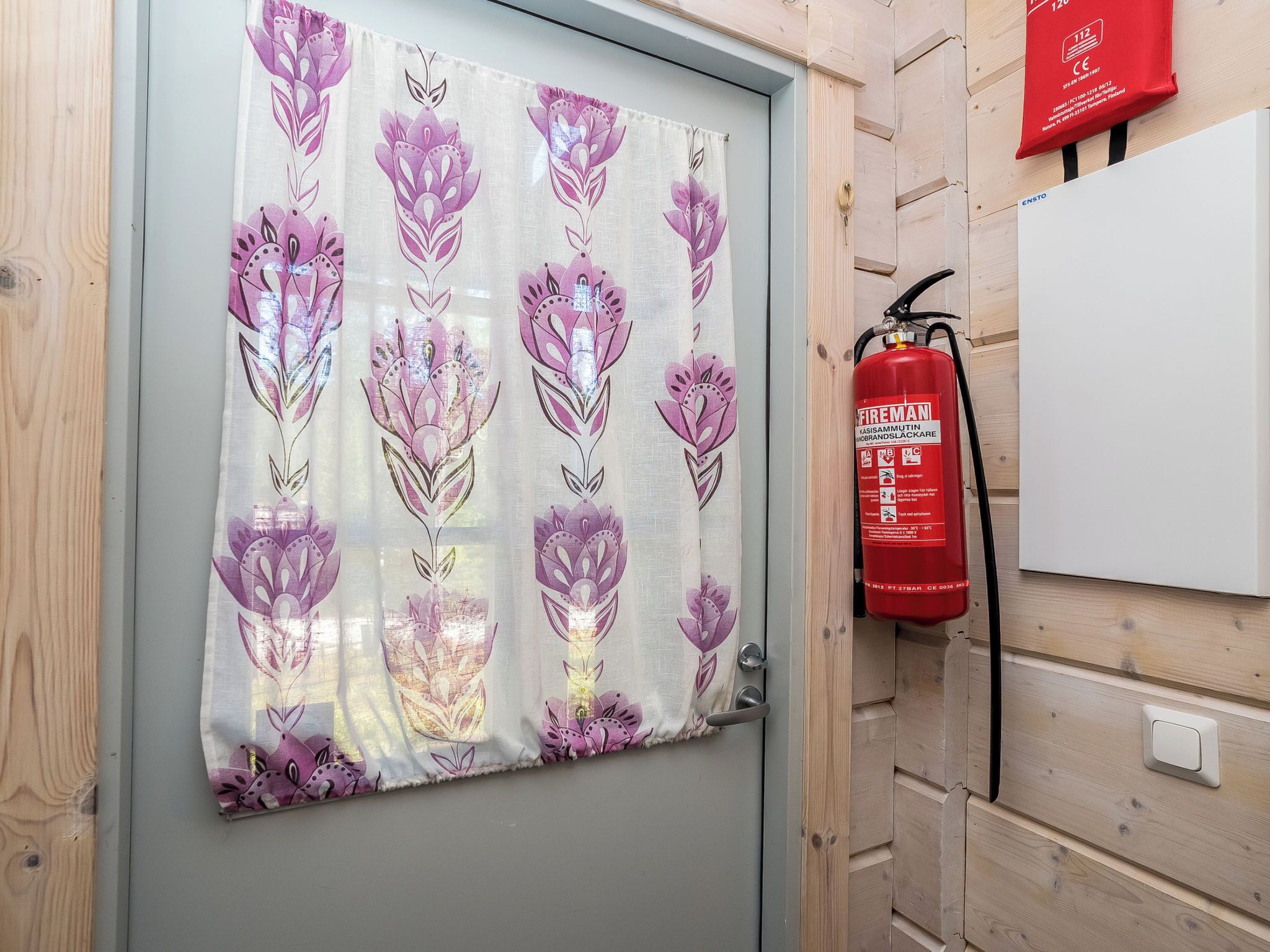 A door with a floral curtain, a fire extinguisher mounted on the wall, and a whiteboard.