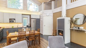 Une cuisine spacieuse dotée d’appareils électroménagers modernes, un coin repas avec des meubles en bois, une cheminée et une mezzanine avec balcon.