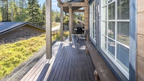 Une terrasse en bois agrémentée d’une pergola, d’un espace salon extérieur et offrant une vue sur une zone boisée.