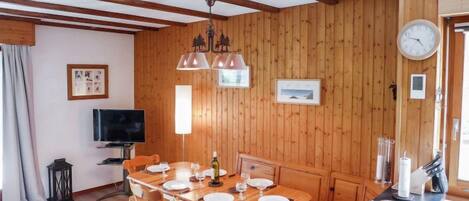 Una habitación con paneles de madera, una mesa de comedor para cuatro personas, un televisor y un reloj en la pared.