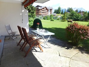 An outdoor patio with a table and chairs, a small garden, and a view of a mountain and buildings in the background.