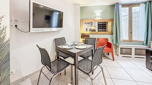 A dining area with a TV mounted on the wall, a table with chairs, and a window with curtains. - Le Sefcotel (Val Claret) by Interhome (Tignes)