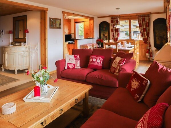 A cozy living room with a red sofa, wooden coffee table, and a dining area with a wooden table and chairs.