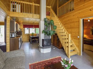 A spacious wooden interior with a central fireplace, a dining area, and a staircase leading to an upper level. - Sointukallio by Interhome (Savonlinna)