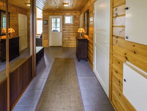 Un couloir intérieur aux murs en bois, agrémenté d’un tapis, d’un banc et d’une lampe.