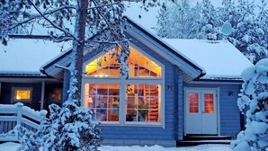 Una casa con techo inclinado y ventanas amplias, rodeada de árboles cubiertos de nieve.