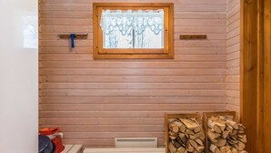 A wooden cabin interior with a window, a table with firewood, and a white bench.