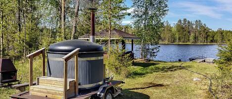 Een draagbare grill met een houten constructie en wielen, op een gazon vlakbij een waterpartij.