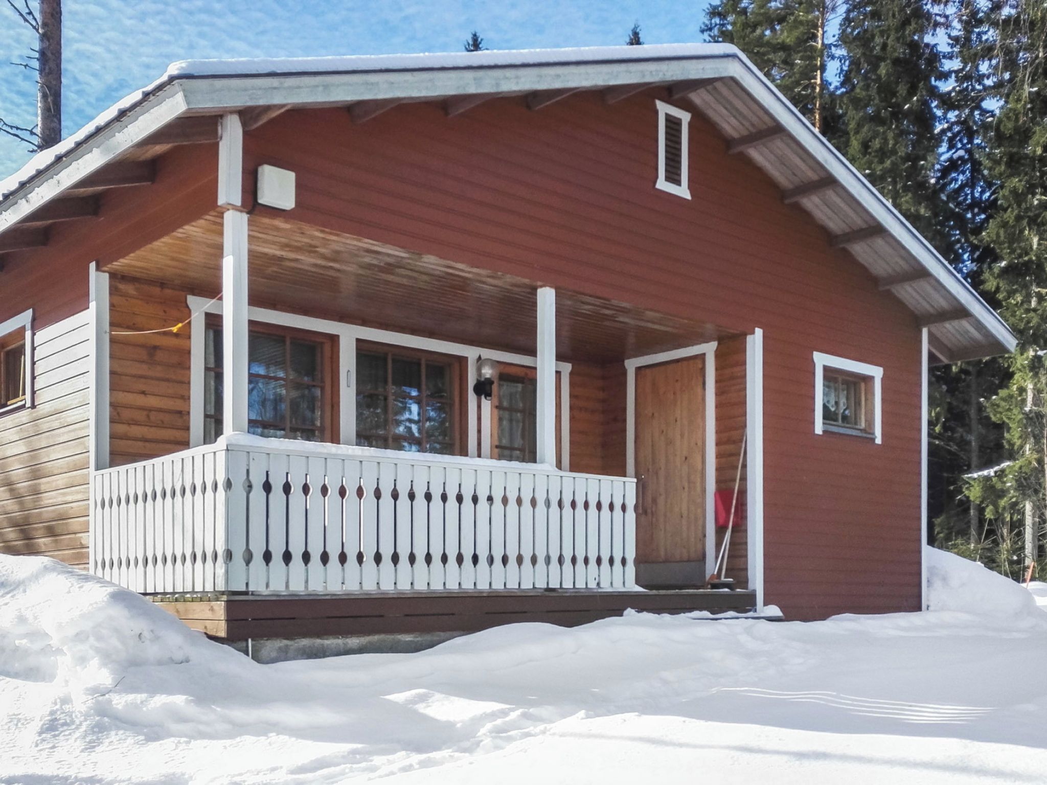 A wooden cabin with a porch and a door, surrounded by snow.