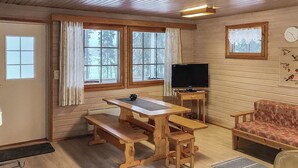 A cozy cabin interior with a wooden table, benches, a television, and a sofa.