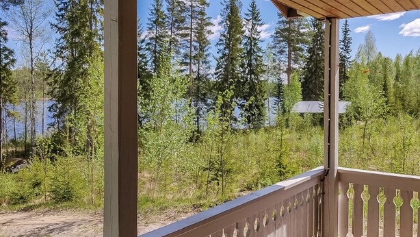 A wooden deck with a railing overlooking a forested area and a body of water.