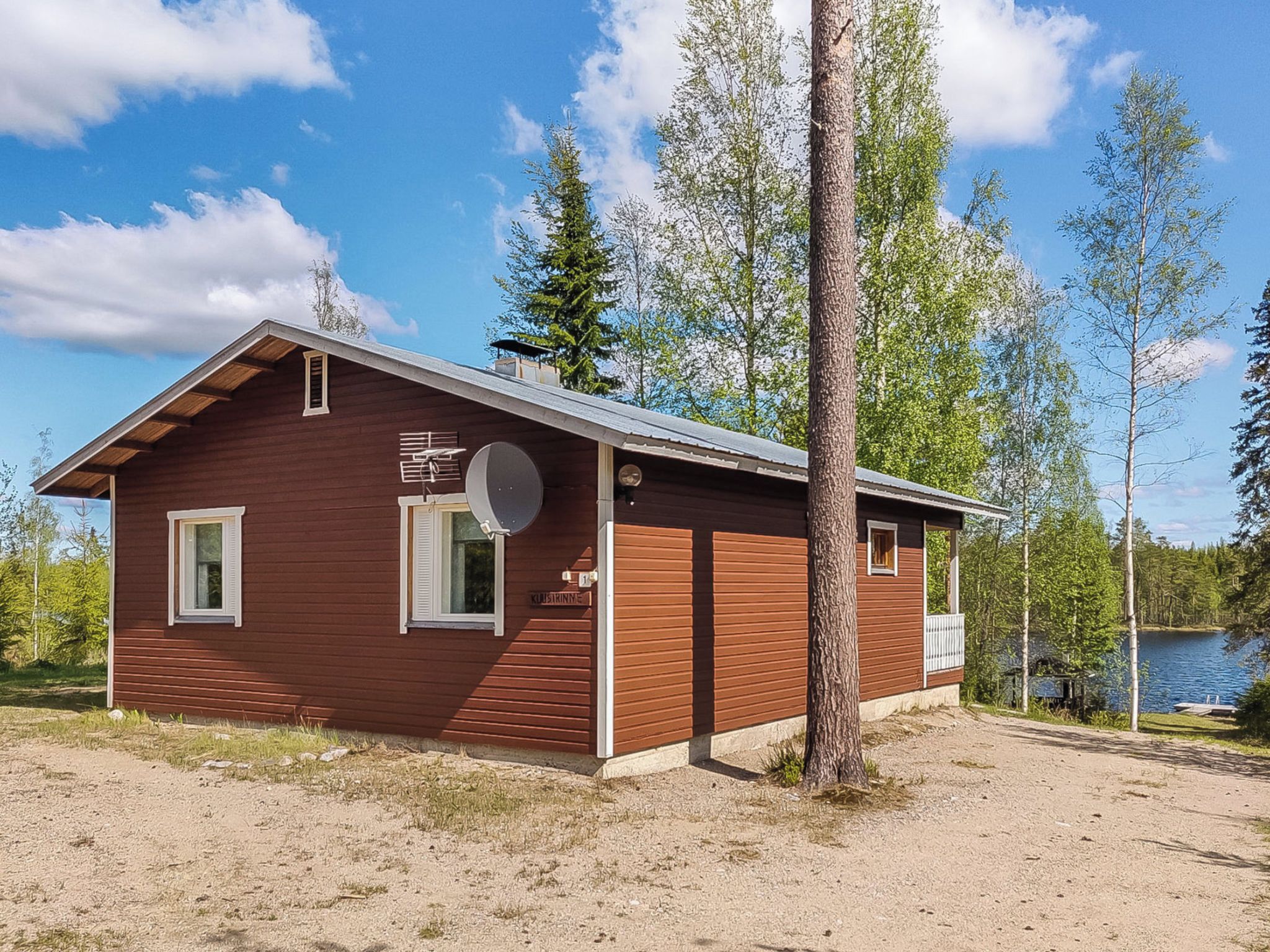 A small wooden cabin with a sloped roof, a satellite dish, and a sign that reads 'Kastirinne.'