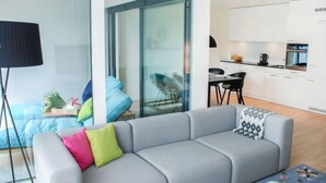 A modern living room with a grey sofa, a small table, and a glass door leading to a kitchen area. - LaVille A-3-4 by Interhome (Locarno)