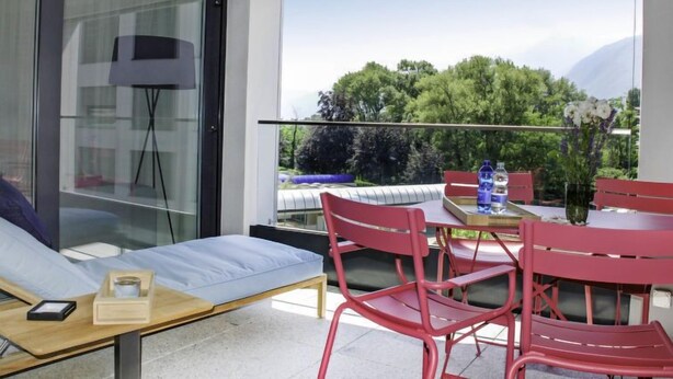 A modern balcony with a sofa, red chairs, and a table with a vase of flowers. - LaVille A-3-4 by Interhome (Locarno)