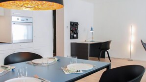 A modern kitchen with white cabinets, a built-in oven, and a dining area with a blue table set for four. - LaVille A-3-4 by Interhome (Locarno)