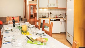 A dining area with a table set for four, a kitchen with white cabinets and appliances, and a living room with a sofa and a fireplace. - Mont-Fort 51 by Interhome (Siviez-Nendaz)