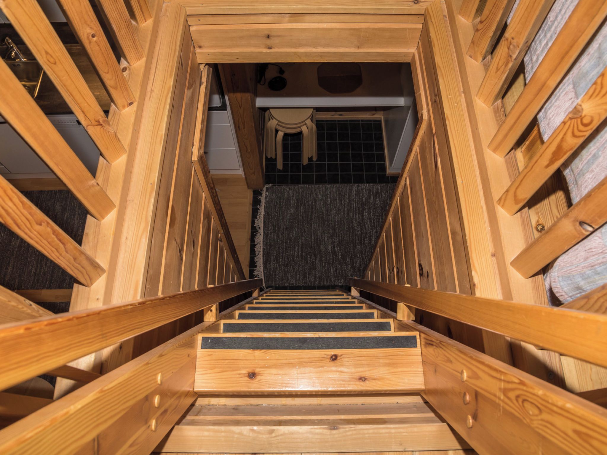 A wooden staircase with a handrail, leading to a room with a tiled floor and a window.