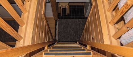 A wooden staircase with a handrail, leading to a room with a tiled floor and a window.