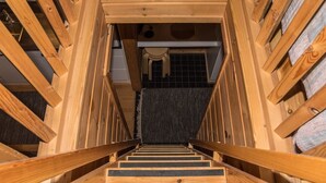 Una escalera de madera con barandilla que lleva a una habitación con pared de azulejos y un ventanal.