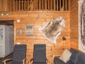 Una habitación con paredes de madera, un manto de piel, dos sillas grises, una cama de madera y una lámpara.
