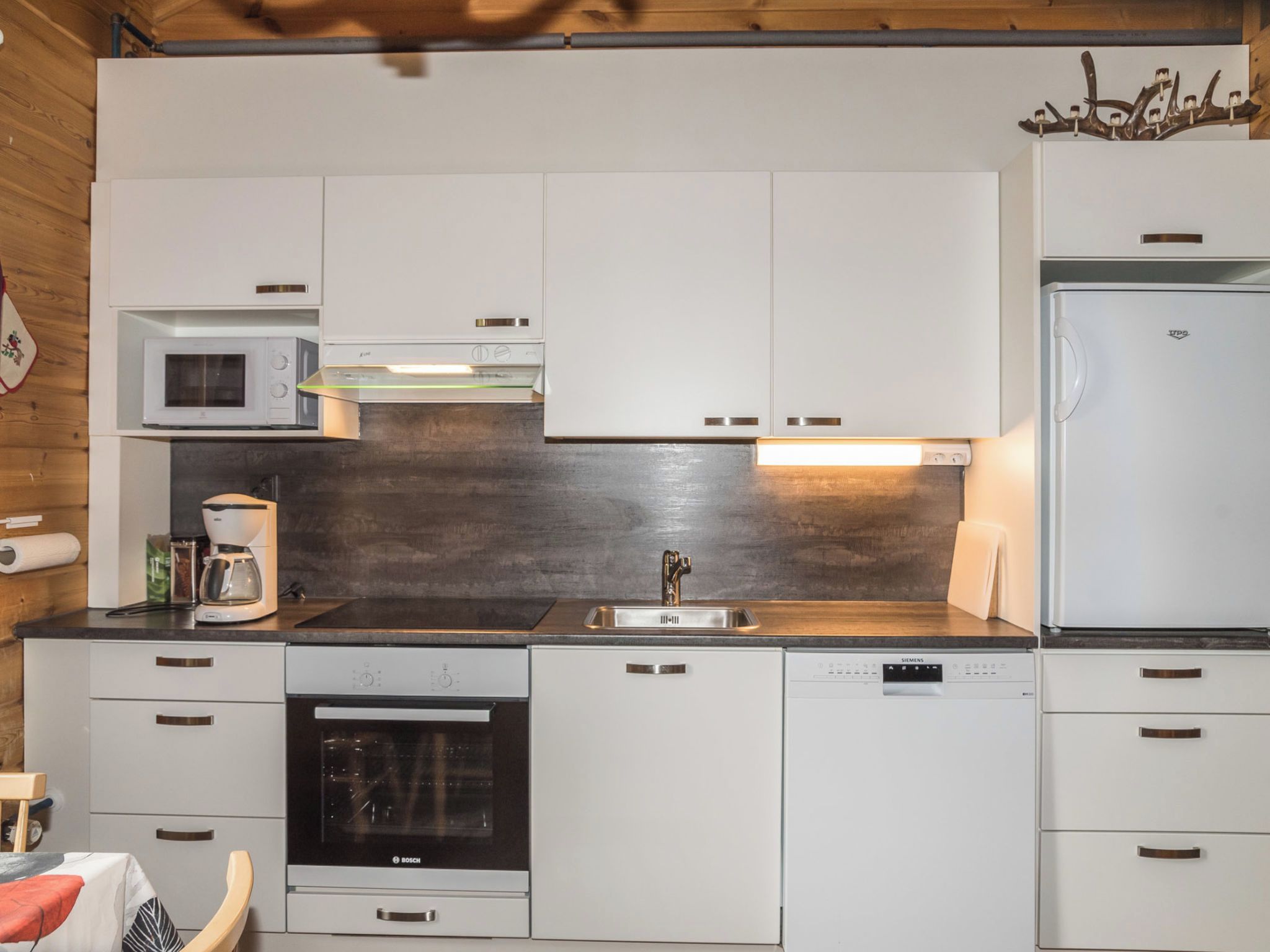 Una cocina moderna con armarios blancos, un horno Bosch, un lavavajillas Siemens y un microondas.