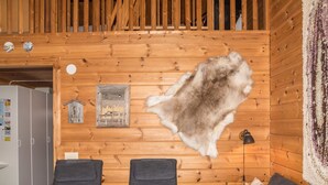 Una habitación con paredes de madera, un pelaje colgado, dos sillas grises, un banco de madera y un pequeño adorno en la pared.