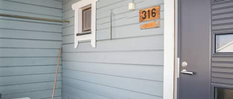 A wooden bench, a broom, a window, and a door with a number plate.
