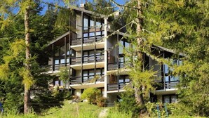 Ein mehrstöckiges Gebäude mit Balkonen, umgeben von dichtem Wald.