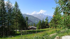 Eine ländliche Berglandschaft mit einem Haus, umgeben von Bäumen und freiem Blick auf ferne Berge.