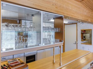 A kitchen with a wooden ceiling, a glass display case with glassware, and a wooden table with a magazine.