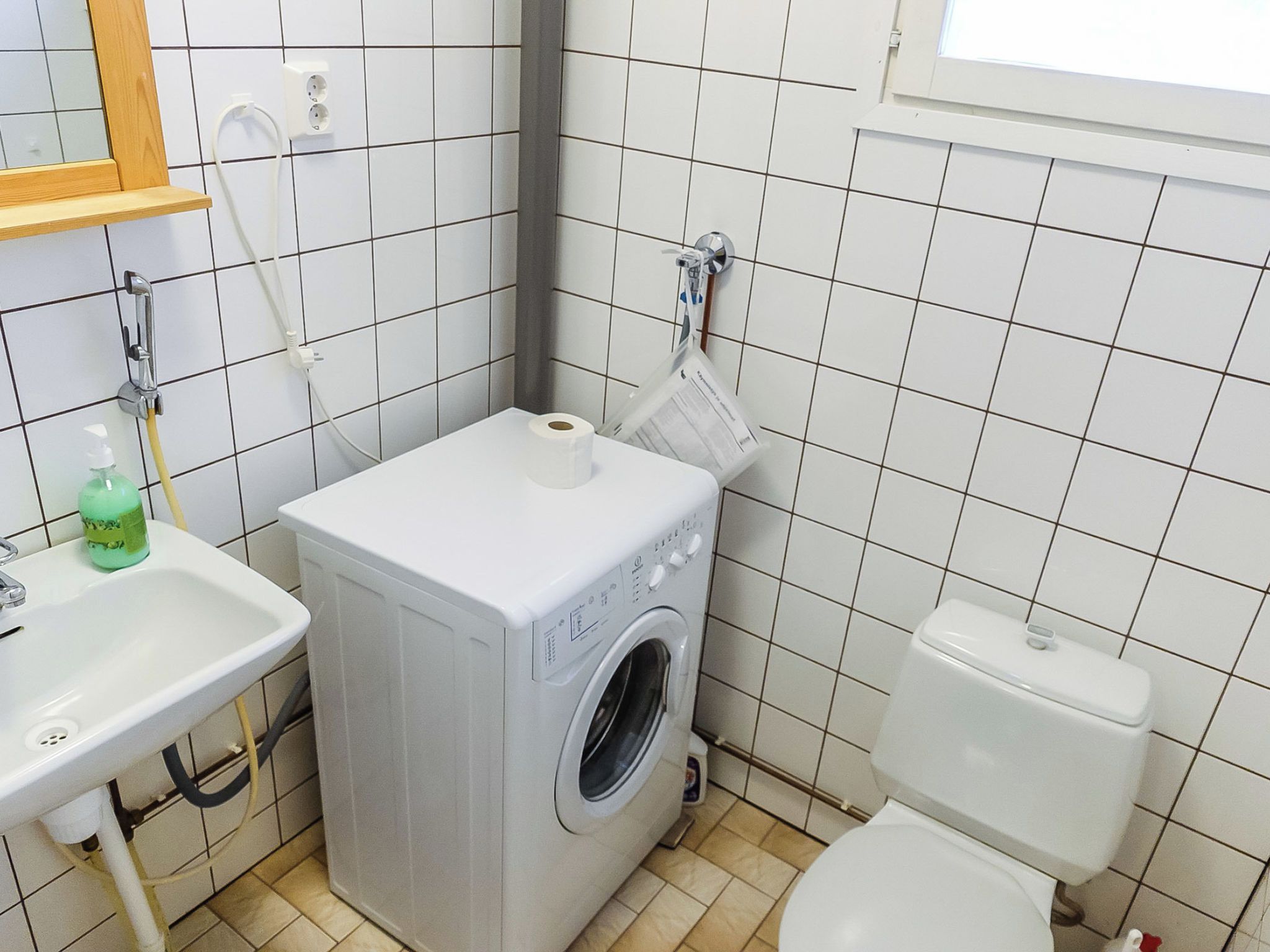 Une petite salle de bain équipée d’un lave-linge, de toilettes, d’un lavabo et d’un miroir.