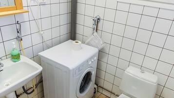 Une petite salle de bain équipée d’un lave-linge, de toilettes, d’un lavabo et d’un miroir.