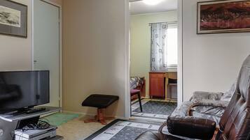 Un soggiorno con televisione, un divano in pelle, un tavolino e uno specchio che riflette un bagno.