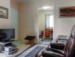 Een woonkamer met een televisie, een leren bank, een bijzettafeltje en een spiegel die een badkamer weerspiegelt.