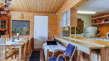 A wooden interior with a dining table, chairs, a bench, a bed, and a kitchen area.
