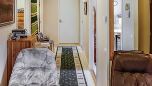 A hallway with a patterned rug, a brown leather chair, a wooden cabinet with books, and a small table with a phone and remote controls. - Itätullinkievari by Interhome (Salla)