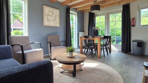 A modern living room with a round wooden coffee table, two sofas, a dining table with chairs, and large windows with curtains. - Zeeuwse Cottage Wemeldinge by Interhome (Wemeldinge)