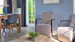 A modern living room with a high ceiling, a dining area with a wooden table and chairs, and a large window with curtains. - Zeeuwse Cottage Wemeldinge by Interhome (Wemeldinge)