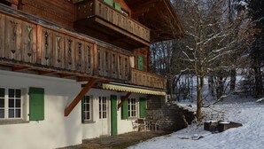 Tipico chalet in legno con balcone, pareti bianche e persiane verdi.