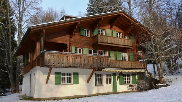 Un chalet in legno a più piani con persiane verdi e balconi, immerso nella neve.
