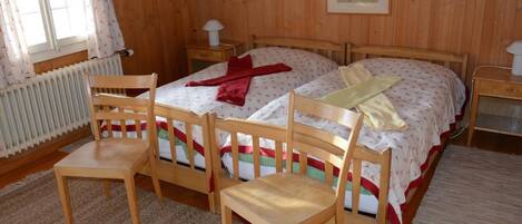 A wooden-paneled bedroom with two single beds, a wooden chair, a bedside table, and a radiator.