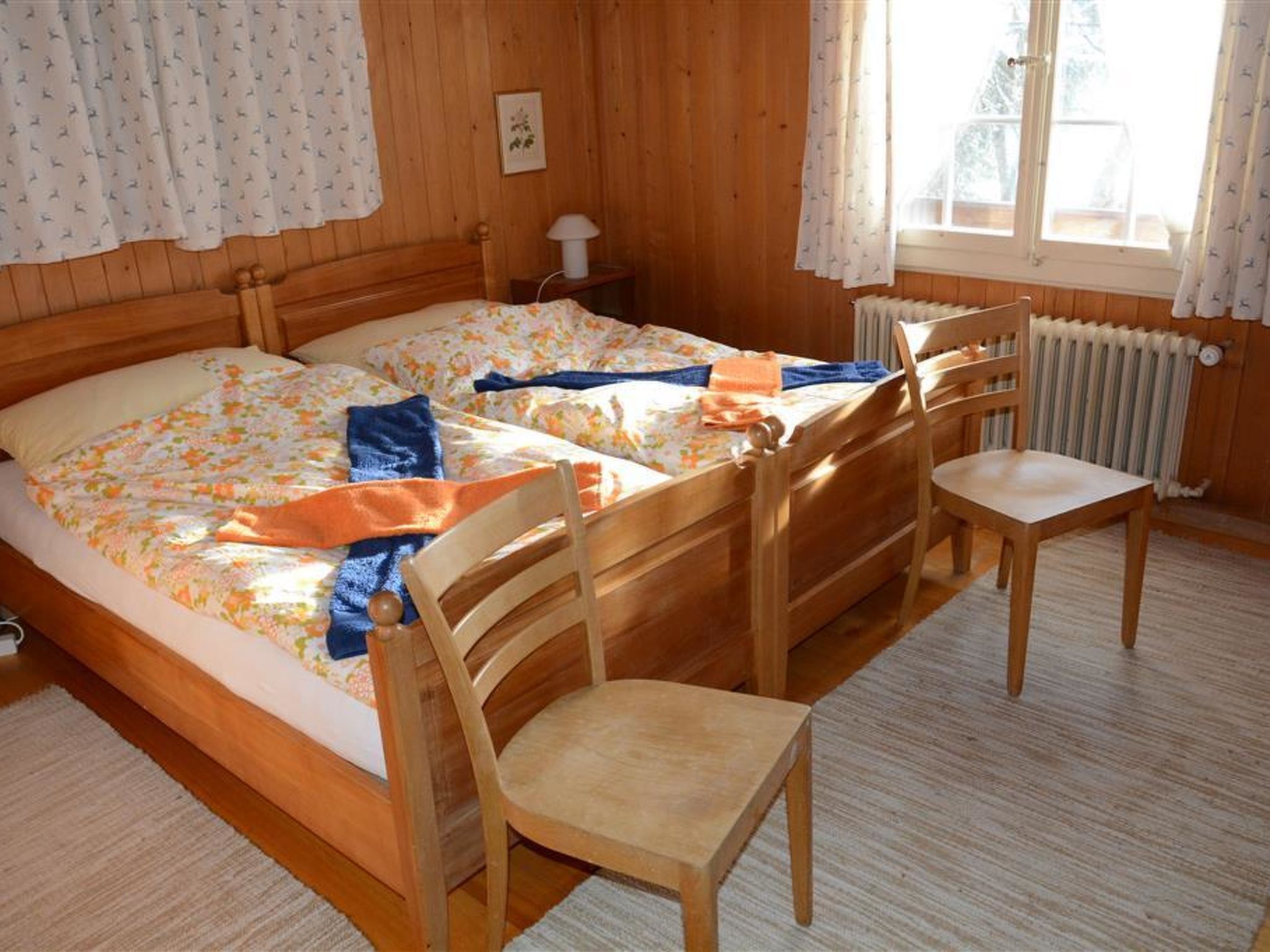 A wooden room with a bed, a chair, a radiator, and a window with curtains.