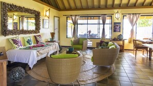 A spacious room with a bed, two wicker chairs, a dining table, and a large window with curtains.