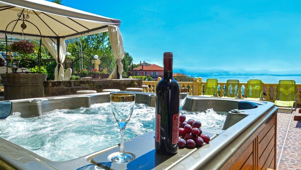 A hot tub with a bottle of wine and a glass, surrounded by lounge chairs, overlooking a scenic view. - Apartment Andrea by Interhome (Opatija/Bregi)