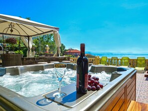 A hot tub with a bottle of wine and a glass, surrounded by lounge chairs, overlooking a scenic view.