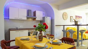 A dining area with a yellow tablecloth, a vase with red flowers, and a clock on the wall. - Apartment Andrea by Interhome (Opatija/Bregi)