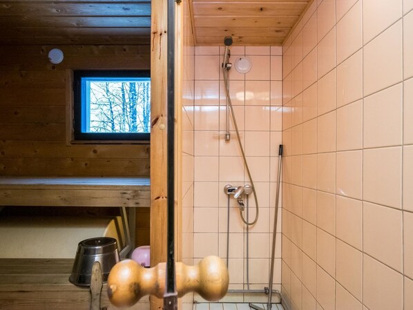 A wooden cabin bathroom with a shower, a window with a view of bare trees, and a wooden floor.