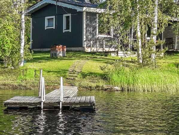 Une maison avec un quai s’avançant dans une étendue d’eau calme, entourée de verdure.